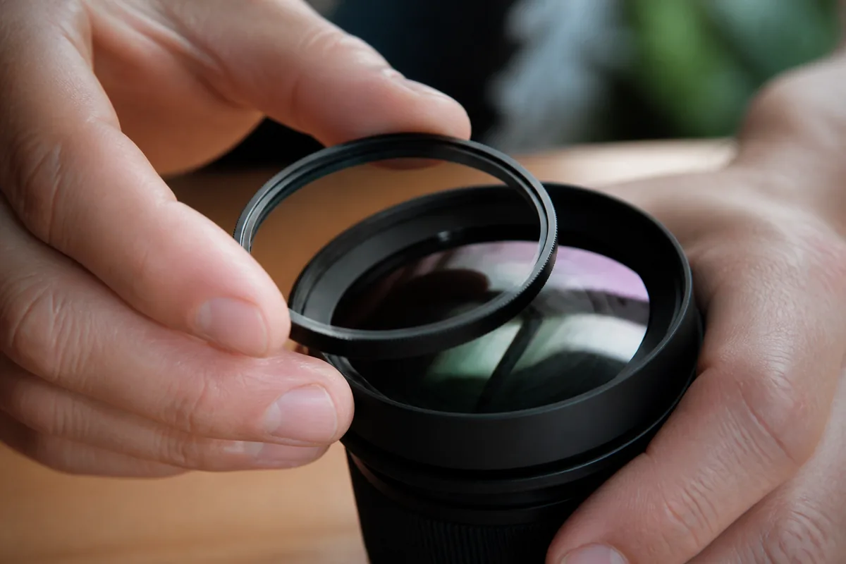 Mains vissant un anneau de verre sur la face avant d&rsquo;un objectif, gros plan macro, lumière naturelle latérale