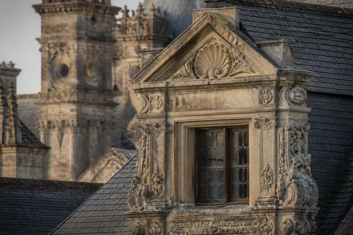 Détail d’une lucarne sculptée et de toitures en ardoise cadré au téléobjectif