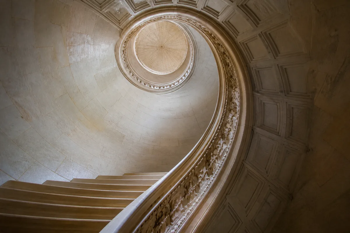 Escalier de pierre en spirale photographié en contre-plongée dans une lumière douce