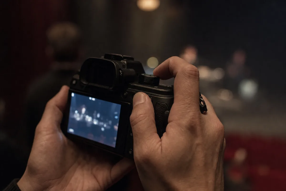 Photographe réglant les molettes de son boîtier plein format dans la pénombre d&rsquo;une salle de spectacle