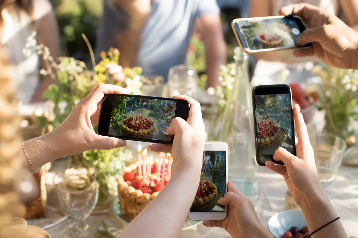 Invités photographiant un gâteau d&rsquo;anniversaire au smartphone dans un jardin ensoleillé